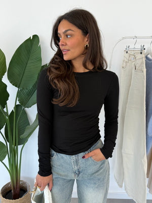 Nyra longsleeve – zwarte, strakke longsleeve met aansluitende pasvorm, model kijkt iets naar de zijkant, vooraanzicht