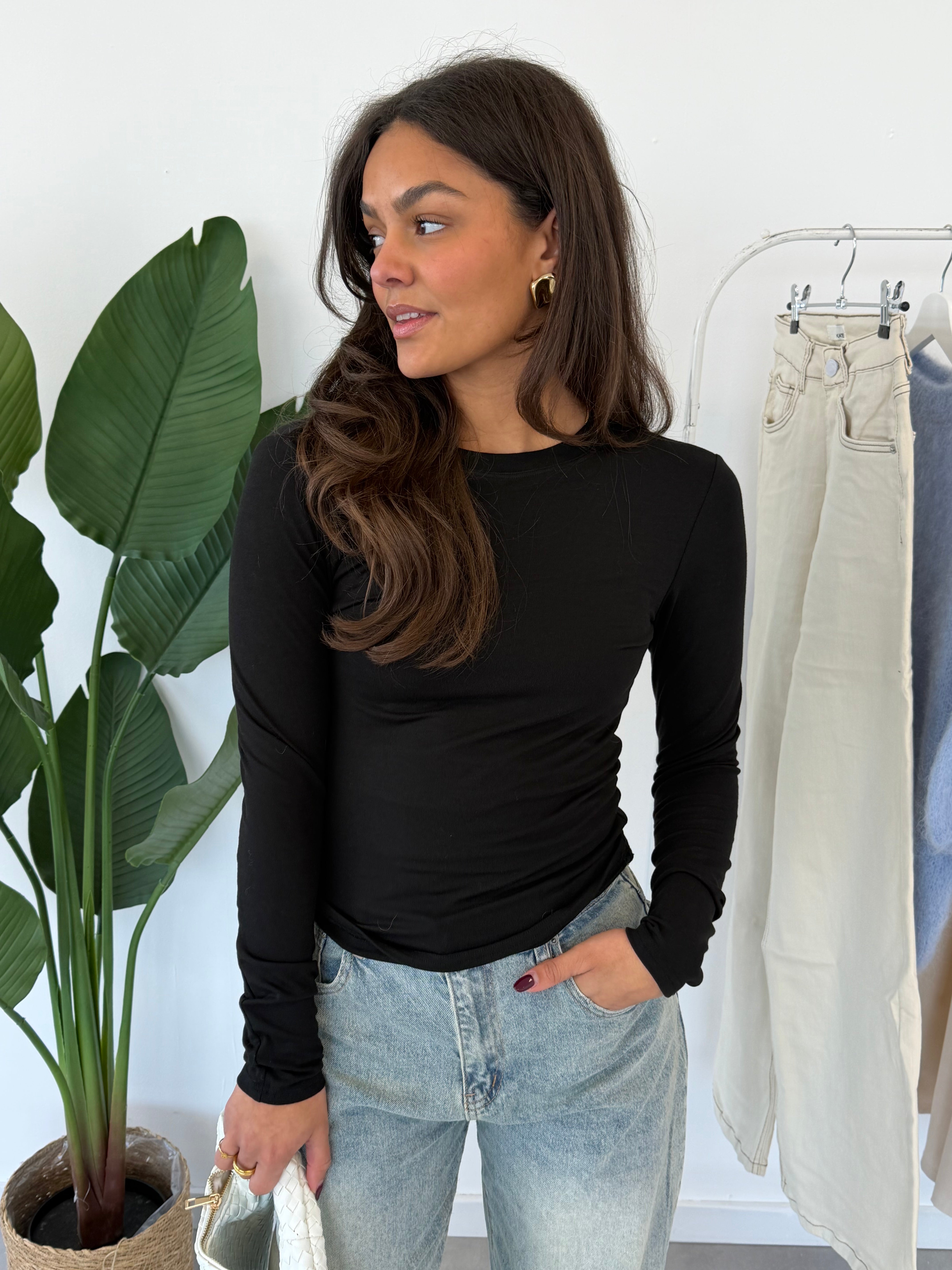 Nyra longsleeve – zwarte, strakke longsleeve met aansluitende pasvorm, model kijkt iets naar de zijkant, vooraanzicht